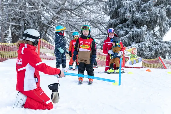 Skilehrerin übt mit einem Kind im Skikindergarten zwischen bunten Stangen
