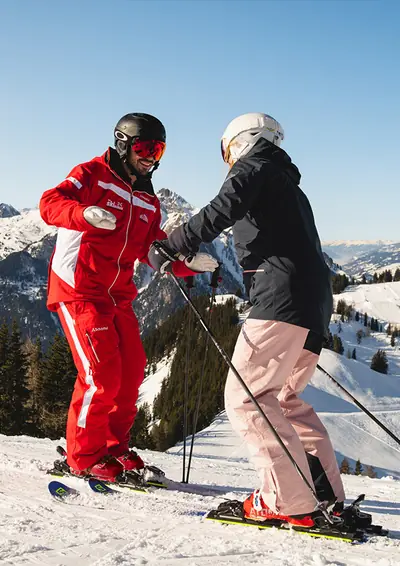 Skilehrer und Schülerin üben gemeinsam auf der Piste vor dem Bergpanorama