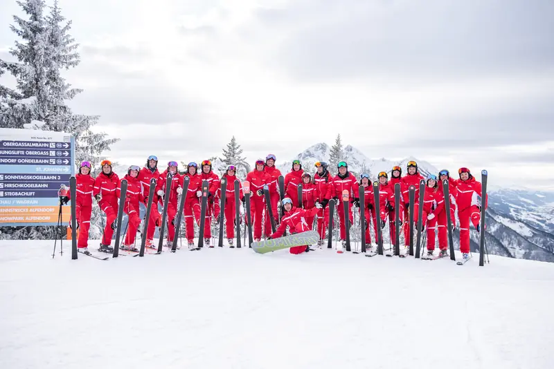Skilehrerinnen und Skilehrer der Skischule Rot-Weiss-Rot stehen in einer Reihe auf der Piste